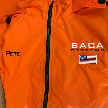Orange BACA Systems windbreaker with embroidered logo, American flag, and employee name